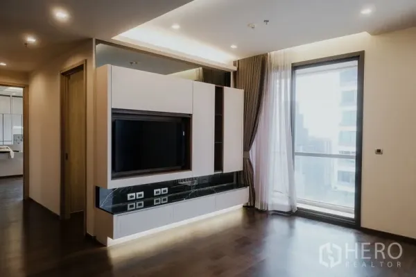 Condominium for rent or sale in Watthana, Bangkok - Bright living area with custom TV wall, floor‑to‑ceiling window and hardwood floors.