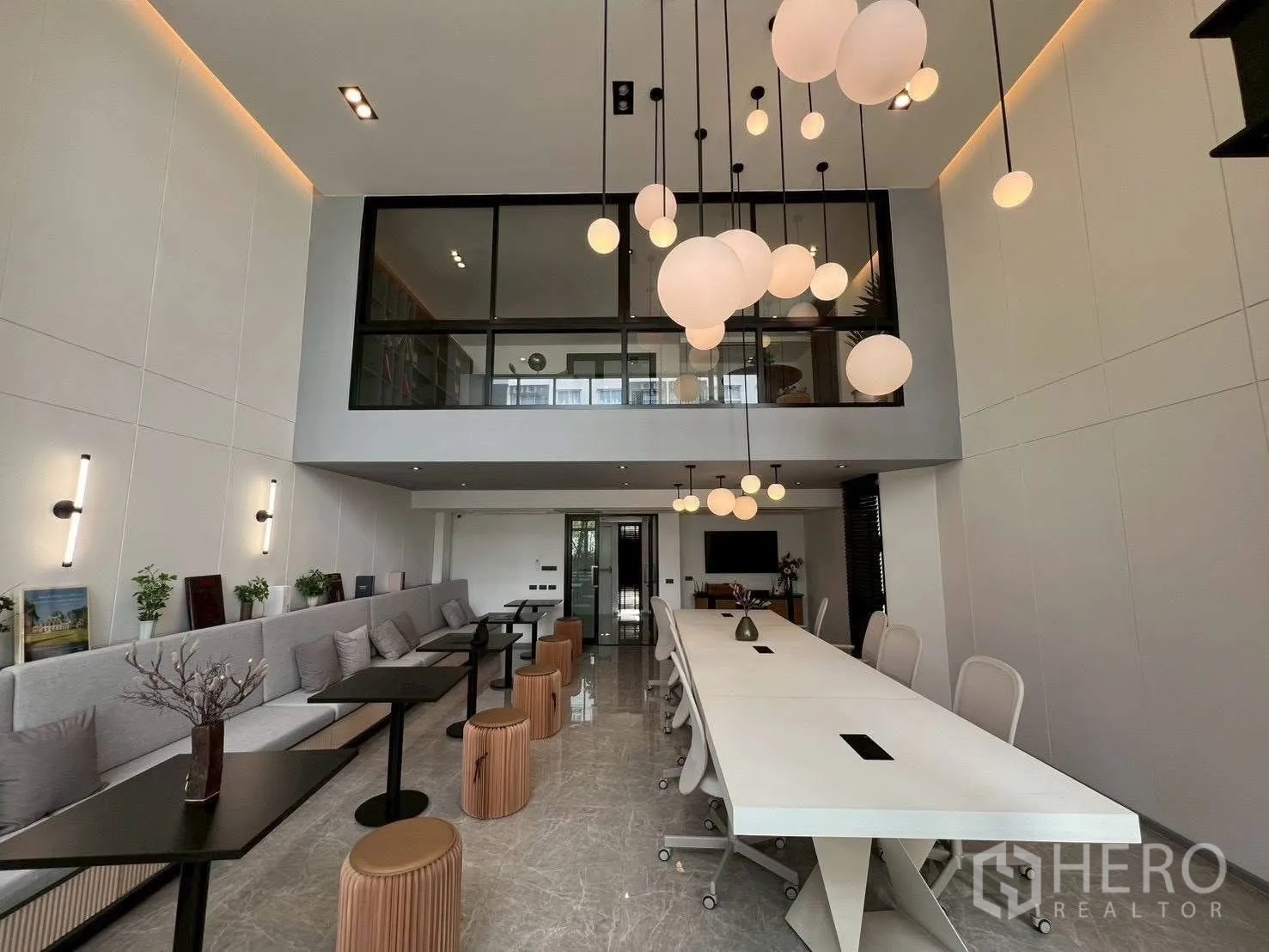 Home Office for rent or sale in Mueang Samut Prakan, Samut Prakan - Double-height coworking hall with long conference table, bench seating and pendant lights.