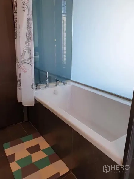 Condominium for rent in Huai Khwang, Bangkok - Bathroom corner featuring a white soaking bathtub with frosted glass partition and patterned mat.