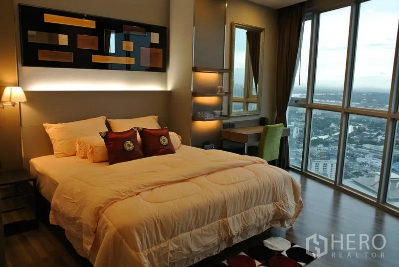 Condominium for rent or sale in Watthana, Bangkok - Spacious master bedroom with large bed, accent wall lighting, work desk, and full-height windows overlooking the city.