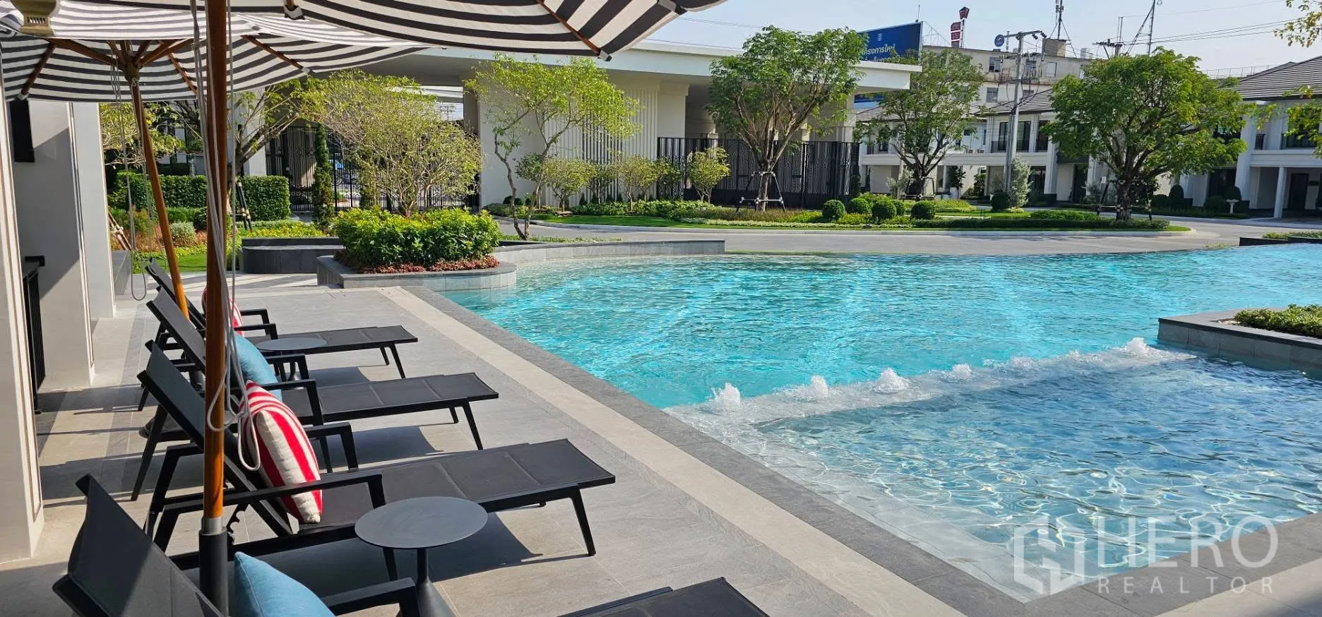 บ้านเดี่ยว for rent or sale in Bang Phli, Samut Prakan - สระว่ายน้ำส่วนกลางสไตล์รีสอร์ท พร้อมเตียงอาบแดดและร่มลายทาง