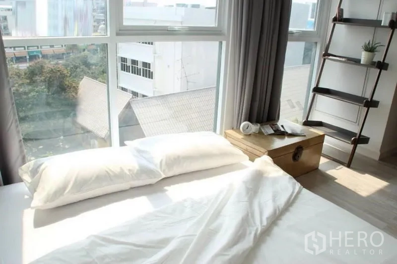 公寓 出售在Phra Khanong, Bangkok - 卧室采光充足，转角落地窗与城市景观，配灰色窗帘。