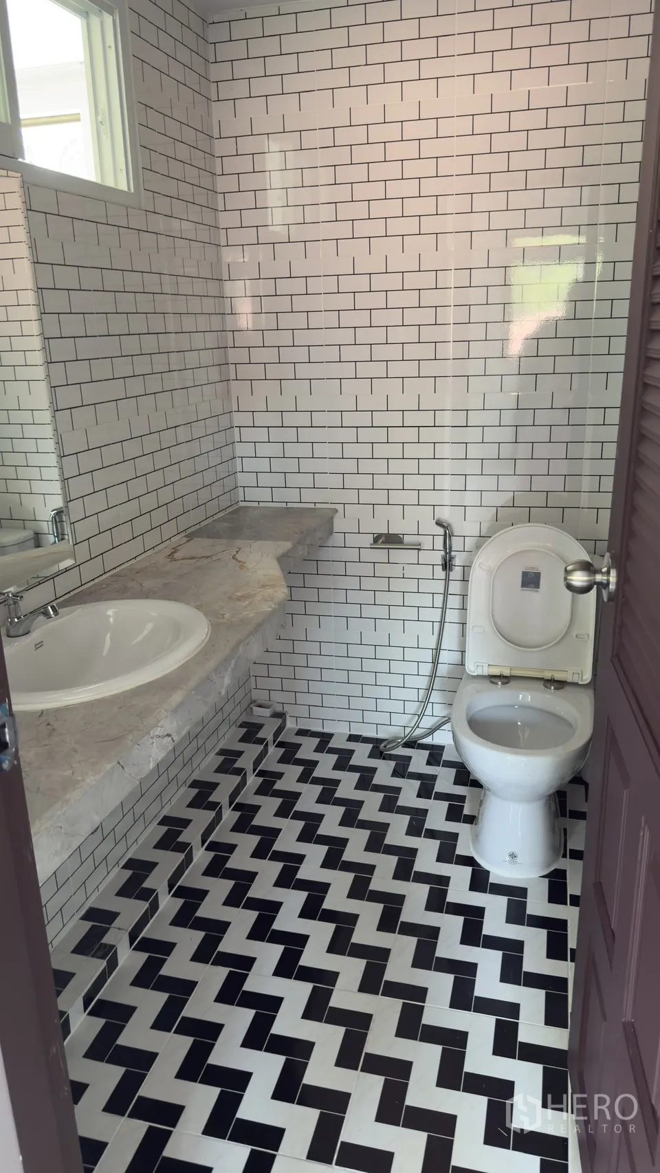 ทาวน์เฮาส์ for rent in Watthana, Bangkok - ห้องน้ำขนาดกะทัดรัด ผนังกระเบื้องลายอิฐ พื้นลายขาวดำ เคาน์เตอร์หินอ่อน และโถสุขภัณฑ์พร้อมสายฉีด