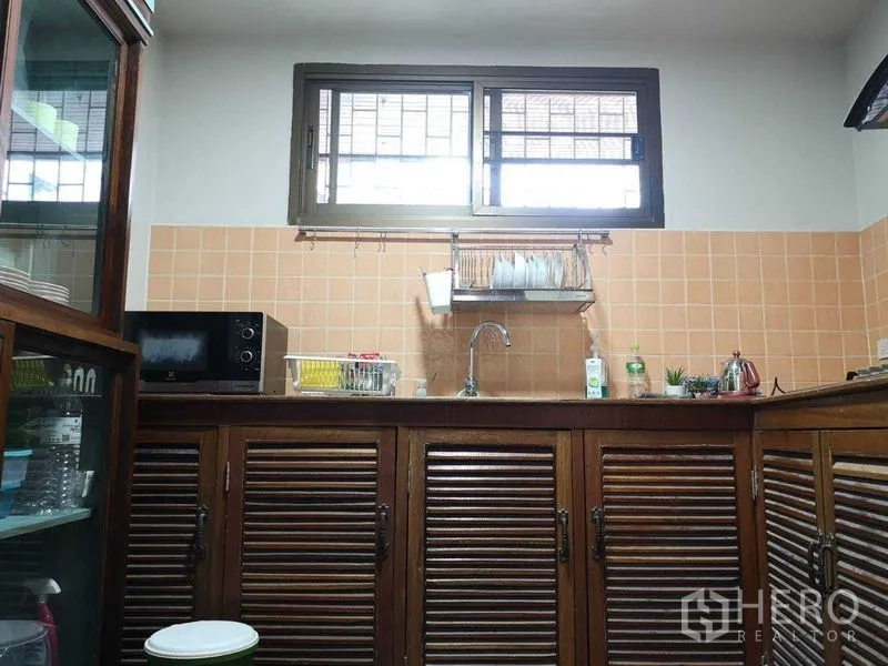 Townhouse for rent or sale in Suan Luang, Bangkok - Thai-style kitchen with wooden louver cabinets, tiled splashback and window.