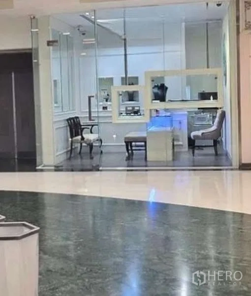 พื้นที่ขายปลีก ให้เช่า - หน้าร้านกระจกภายในศูนย์การค้า ภายในโทนขาว มีตู้โชว์และที่นั่ง