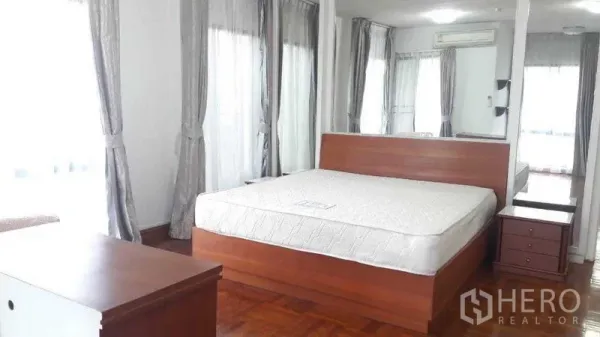 อพาร์ทเมนท์ ให้เช่าในPathum Wan, Bangkok - ห้องนอนใหญ่ เตียงคิง ผนังกระจกหน้าบาน หน้าต่างมุมพร้อมผ้าม่าน และพื้นไม้