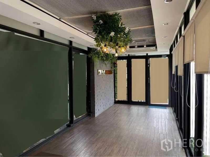 零售空间 出租在Watthana, Bangkok - 明亮的商铺室内，木地板、玻璃门面、悬挂绿植与卷帘。