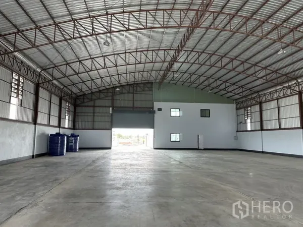 工厂 出租或出售在Sai Noi, Nonthaburi - 仓库内部高拱形钢桁架屋顶，抛光混凝土地面与卷帘门。