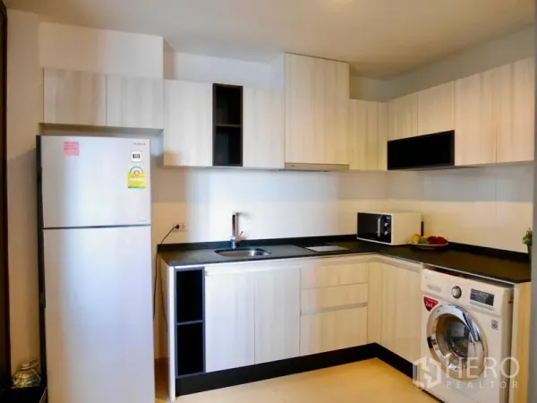 公寓 出租在Watthana, Bangkok - 现代U形厨房，浅木色橱柜，配备冰箱、灶台、微波炉和洗衣机。