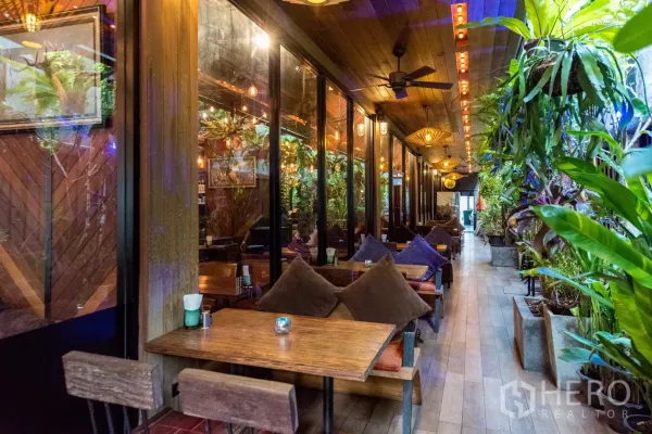 พื้นที่ขายปลีก ให้เช่าในWatthana, Bangkok - ระเบียงนั่งเล่นมีหลังคา โต๊ะไม้ หมอนอิง พัดลมเพดาน และต้นไม้เขียวชอุ่ม