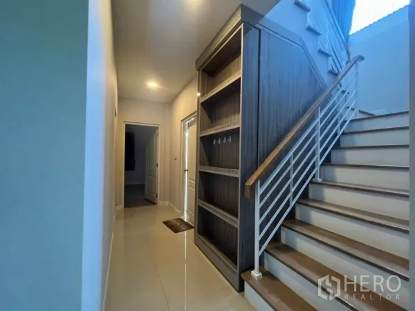 Detached House for rent in Samut Prakan - Hallway and staircase with wooden steps and built-in shelving under the stairs.
