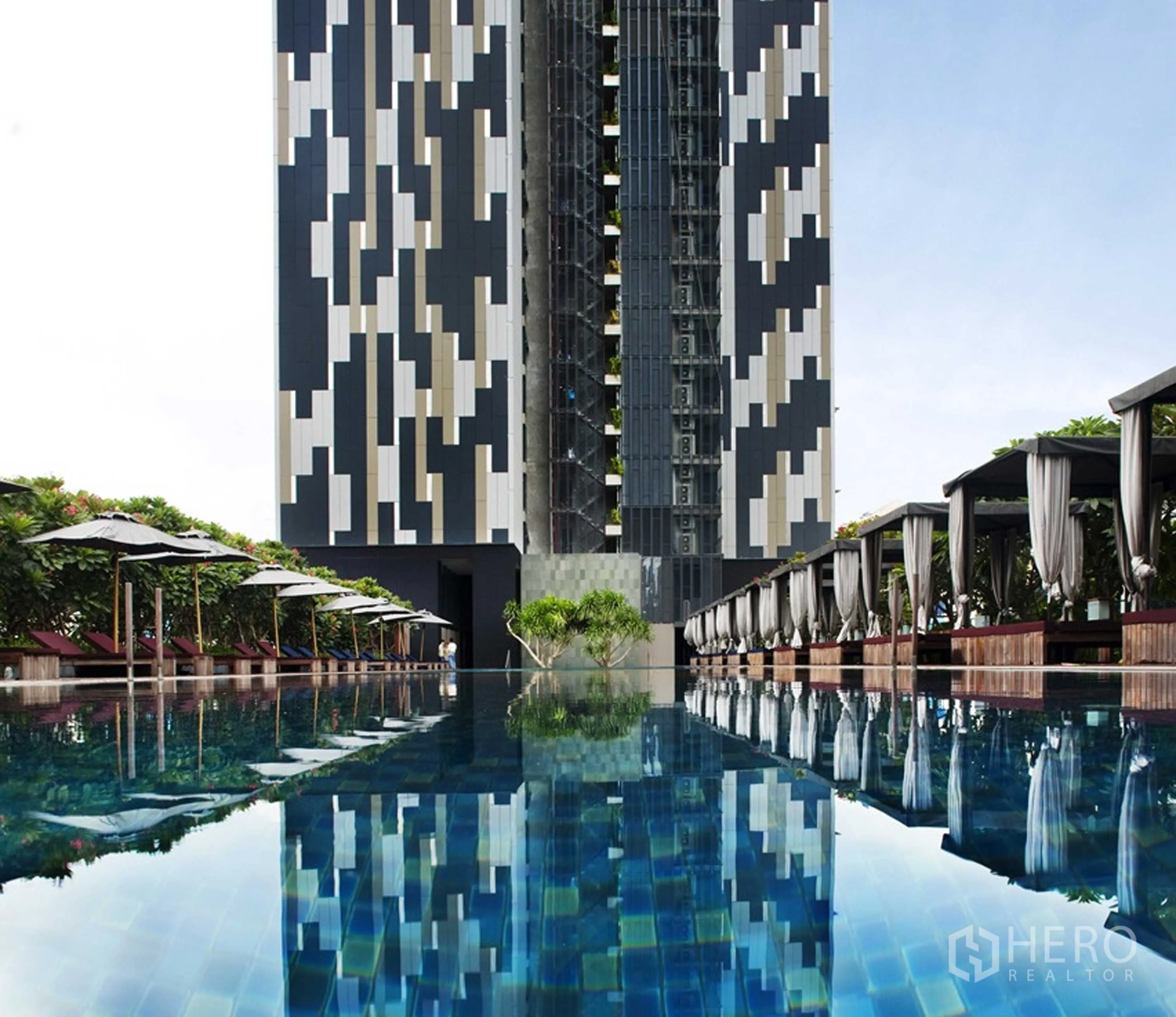 Condominium for rent or sale in Sathon, Bangkok - Resort-style swimming pool with cabanas and high-rise facade reflected on water.