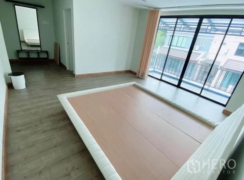 Townhouse for rent in Wang Thonglang, Bangkok - Upper-floor bedroom with platform bed, wood floors, and balcony sliding doors.