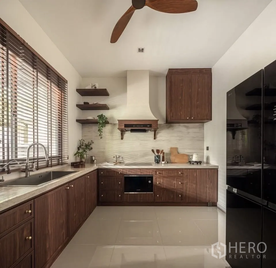 Detached House for rent or sale in Lat Krabang, Bangkok - U-shaped kitchen view with sink, window blinds, ceiling fan, and wood cabinetry.