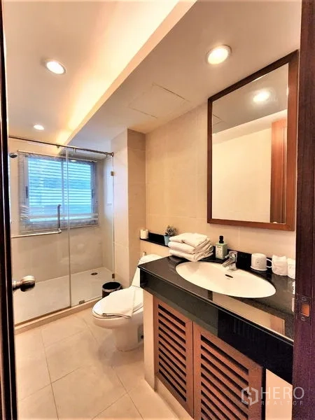 Condominium for rent in Bang Rak, Bangkok - Guest bathroom with walk-in shower, toilet and sleek countertop basin.