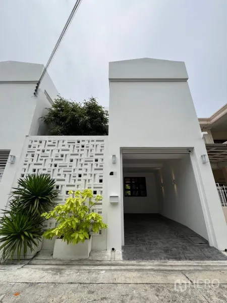 ทาวน์เฮาส์ ขายในWatthana, Bangkok - ด้านหน้าทาวน์เฮ้าส์สองชั้นสีขาวรีโนเวทใหม่ มีกำแพงบล็อกช่องลม ต้นไม้กระถาง และโรงจอดรถมีหลังคา