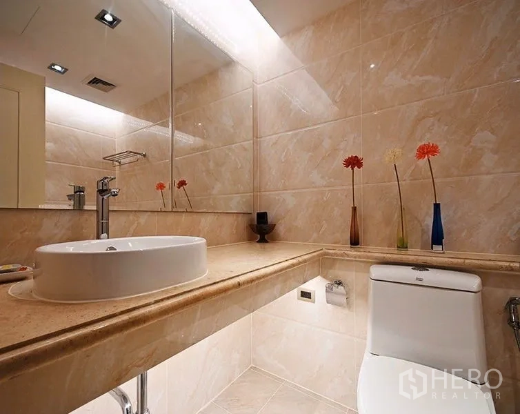 Condominium for rent in Pathum Wan, Bangkok - Guest bathroom finished in beige marble-style tiles with wide mirror and vanity.