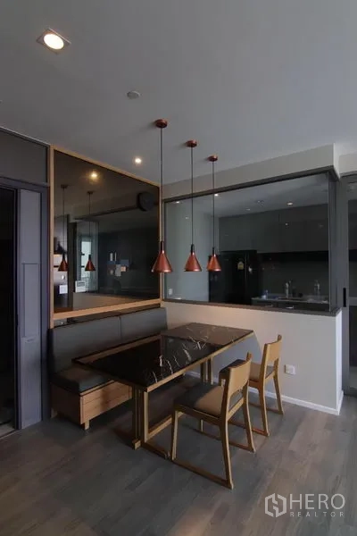 Condominium for rent in Bang Sue, Bangkok - Dining area with marble-top table, bench seating, and pendant lights beside a glass kitchen wall.