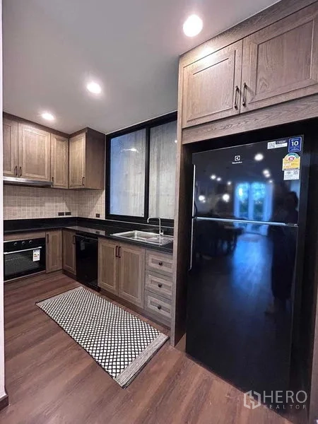 Detached House for rent in Bang Rak, Bangkok - U-shaped kitchen with wood cabinets, black countertops and a large fridge.