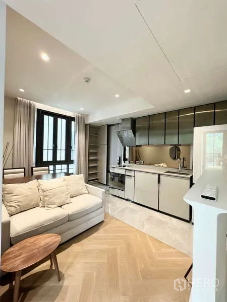 Condominium for rent in Watthana, Bangkok - Bright living room with sofa, open kitchen, and herringbone wood floors at The Reserve Sukhumvit 61.