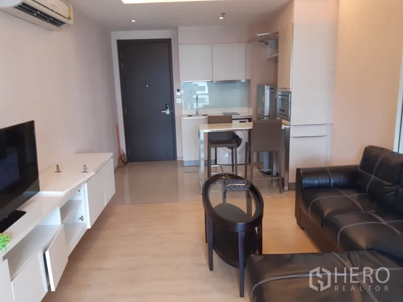 Condominium for rent in Watthana, Bangkok - Open-plan lounge facing a compact kitchen with breakfast counter, modern cabinetry, and the entry door.