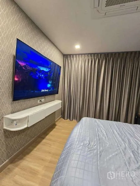 Detached House for rent in Thanyaburi, Pathum Thani - Master bedroom with wall-mounted TV, heavy drapes, wood-look flooring and air conditioning.