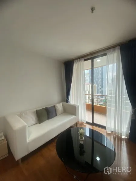 คอนโด ให้เช่าในPathum Wan, Bangkok - ห้องนั่งเล่นสว่างด้วยโซฟาสีขาว โต๊ะกลางทรงกลม และประตูกระจกสไลด์ออกสู่ระเบียงชมวิวสกายไลน์กรุงเทพฯ