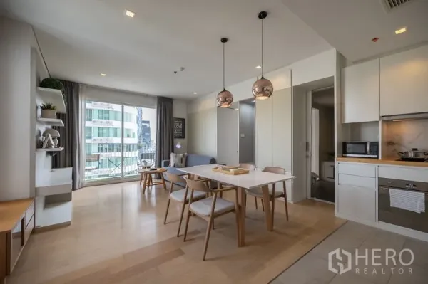 Condominium for rent in Watthana, Bangkok - Bright open-plan living, dining and kitchen with wood floors, pendant lights and balcony access.