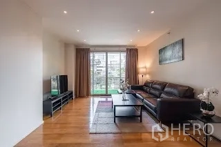 Condominium for rent in Bang Rak, Bangkok - Bright living room with leather sofa, TV console and balcony doors overlooking greenery.