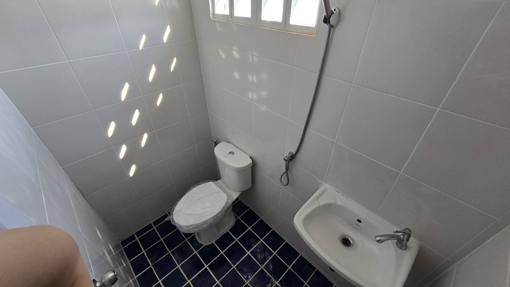 货栈 出租在Bang Phli, Samut Prakan - 仓库内干净的瓷砖卫生间，含坐便器、洗手盆与喷枪。