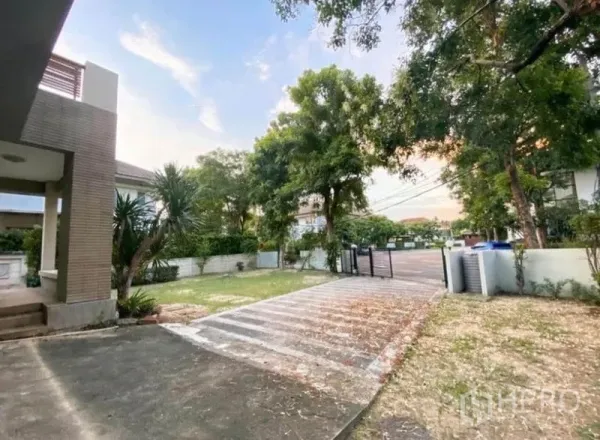 บ้าน ขายในSaphan Sung, Bangkok - ทางรถยนต์กว้างพร้อมประตูรั้ว สนามหญ้าและต้นไม้ใหญ่ในหมู่บ้านเงียบสงบ