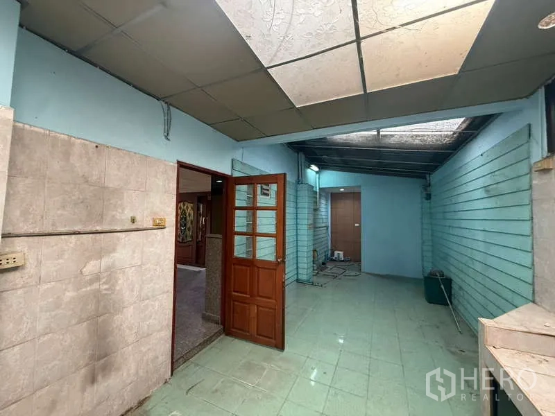 Home Office for rent in Khlong Toei, Bangkok - Semi-outdoor utility area with skylight, mint walls and a wooden door leading to interior rooms.