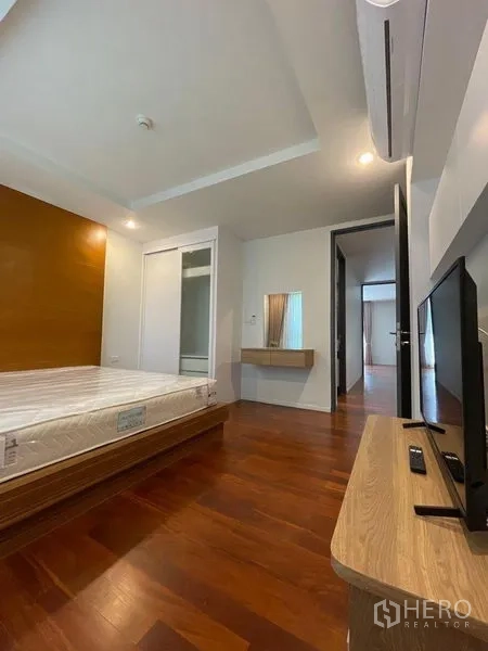 Condominium for rent in Watthana, Bangkok - Bedroom view showing bed, TV console, air conditioner and dressing nook on warm wood flooring.