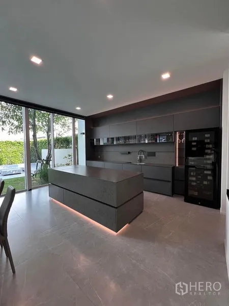 Detached House for sale in Samut Prakan - Sleek open kitchen with an island, dark cabinets, and wine fridge facing garden views.