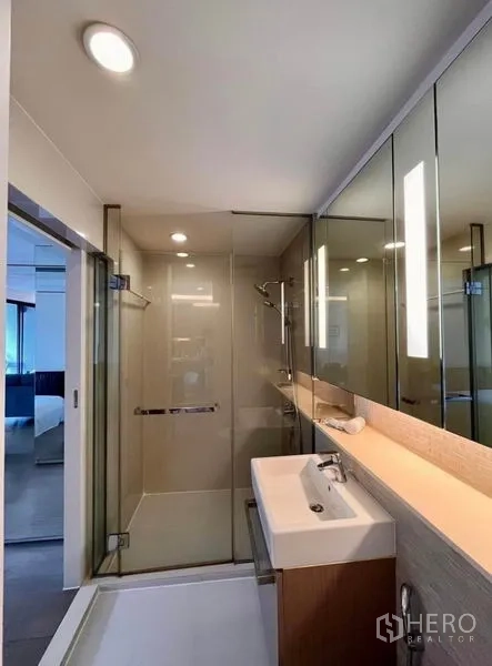 Condominium for rent in Watthana, Bangkok - Contemporary bathroom with glass-enclosed shower, illuminated mirror, and white basin.