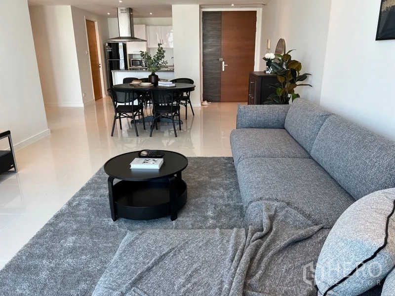 Condominium for rent in Watthana, Bangkok - Spacious living room with gray chaise sofa, round coffee table and outlook toward the dining and kitchen.