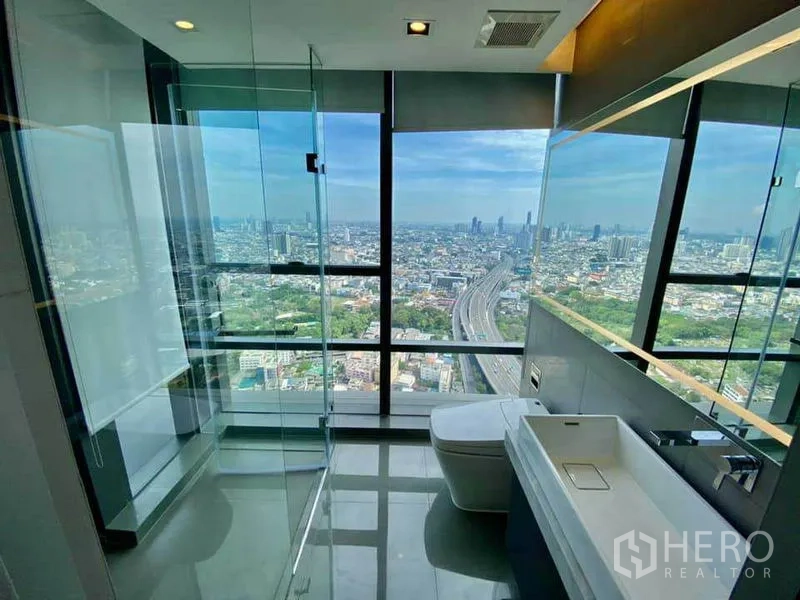 Condominium for rent in Sathon, Bangkok - Bathroom with glass-enclosed shower and sweeping skyline views from full-height windows.