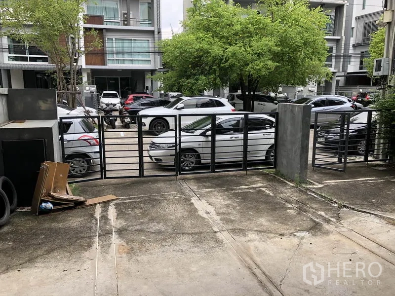 Home Office for rent in Wang Thonglang, Bangkok - Gated driveway and parking area facing a tree-lined private street with several parked cars.