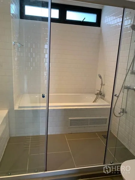 Condominium for rent in Watthana, Bangkok - Bathroom with glass enclosure, white subway tiles and a bathtub with handheld shower.