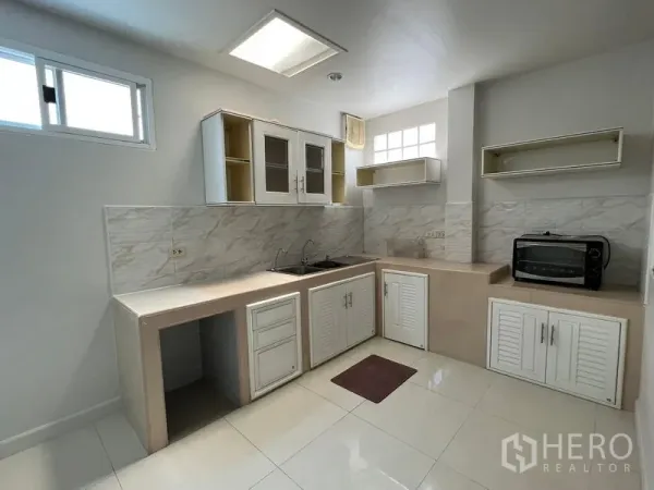 独立式住宅 出租在Bang Kapi, Bangkok - 明亮的L形厨房，白色橱柜、瓷砖墙面与采光窗。