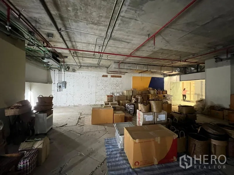 零售空间 出租 - 未完成的店铺空间，开放布局，靠近玻璃走廊处堆放物品。