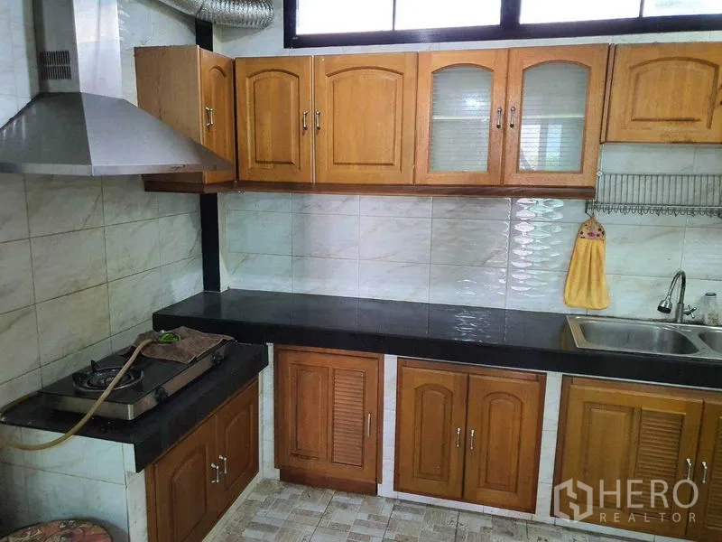 Townhouse for sale in Khlong Toei, Bangkok - Enclosed kitchen with wooden cabinets, black countertops, and range hood.