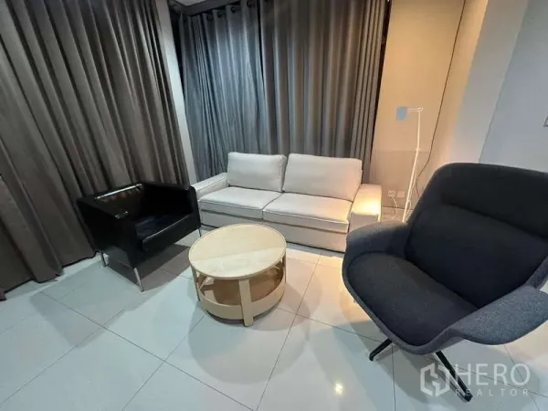 Detached House for rent or sale in Bang Kapi, Bangkok - Cozy living room with sofa set and round coffee table on glossy tile flooring and full-height curtains.