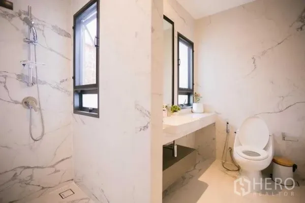 Detached House for rent in Bangkok - Guest bathroom with marble-look tiles, window, wall-mounted vanity and separate shower area.