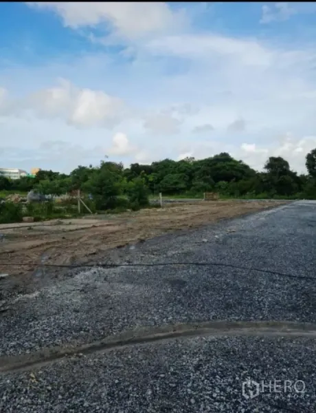 Land for sale in Khlong Toei, Bangkok - Cleared plot with gravel base beside green trees under a bright sky.