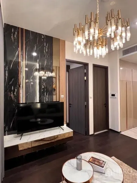 Condominium for rent in Watthana, Bangkok - Black marble TV wall with gold chandelier and dark wood doors in an upscale Bangkok condominium.