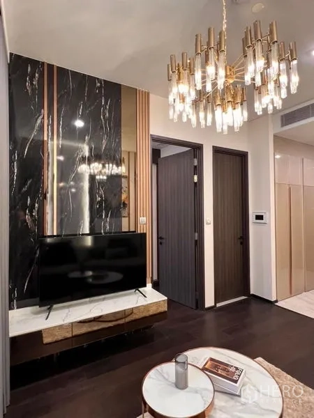 Condominium for rent in Watthana, Bangkok - Black marble TV wall with gold chandelier and dark wood doors in an upscale Bangkok condominium.