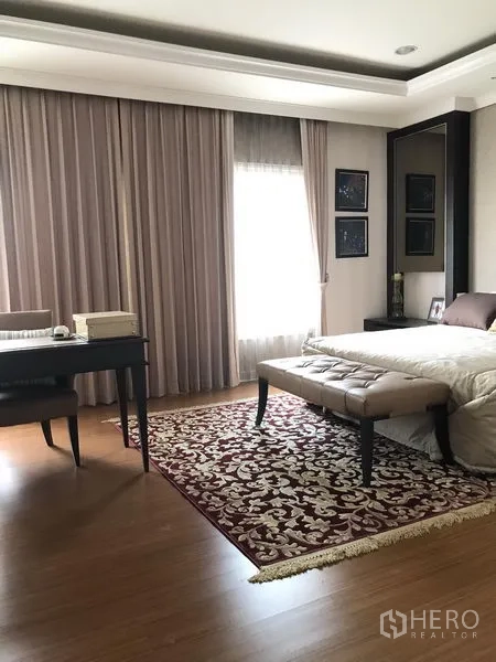 Townhouse for rent or sale in Bang Kho Laem, Bangkok - Spacious bedroom with study desk, bench at the foot of the bed, hardwood floors and patterned rug.