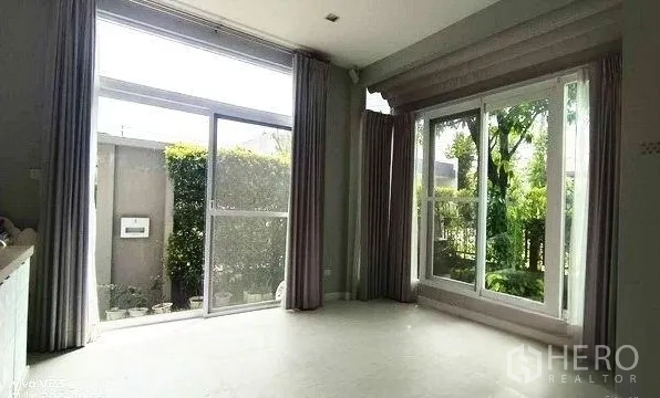 Detached House for rent in Don Mueang, Bangkok - Living room featuring floor-to-ceiling sliding glass doors that open to a small garden.