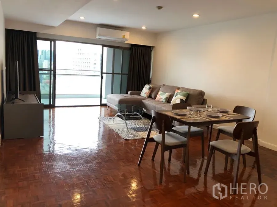 Condominium for rent or sale in Sathon, Bangkok - Bright living and dining area with L-shaped sofa, set table, TV stand and sliding doors to a balcony with city view.